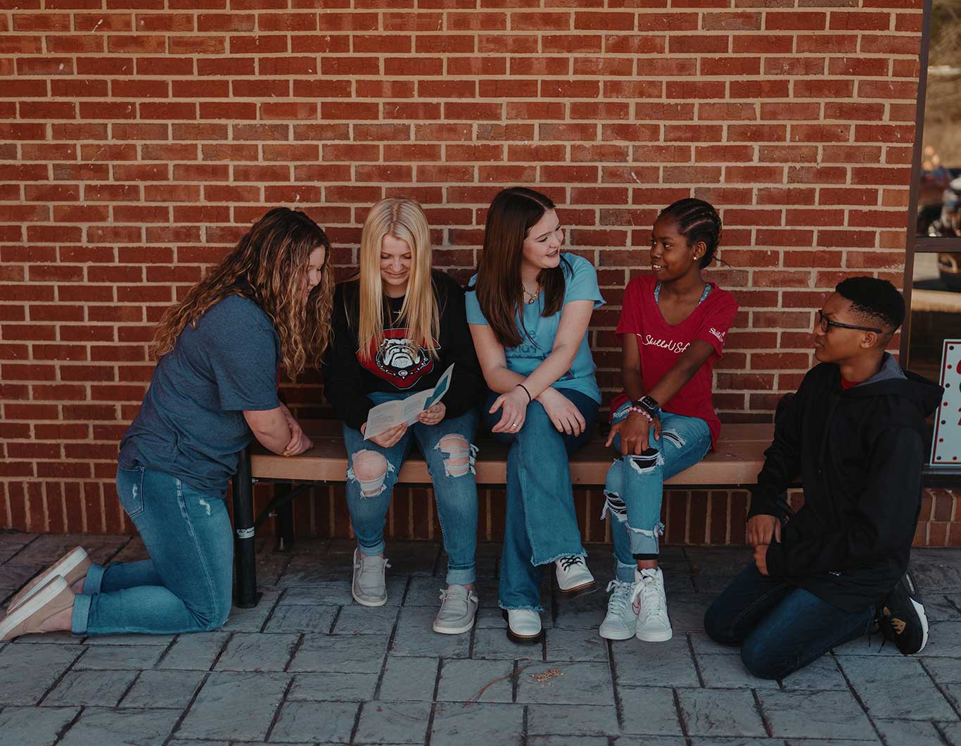 Photo of a group of young students on a bench in front of a school.