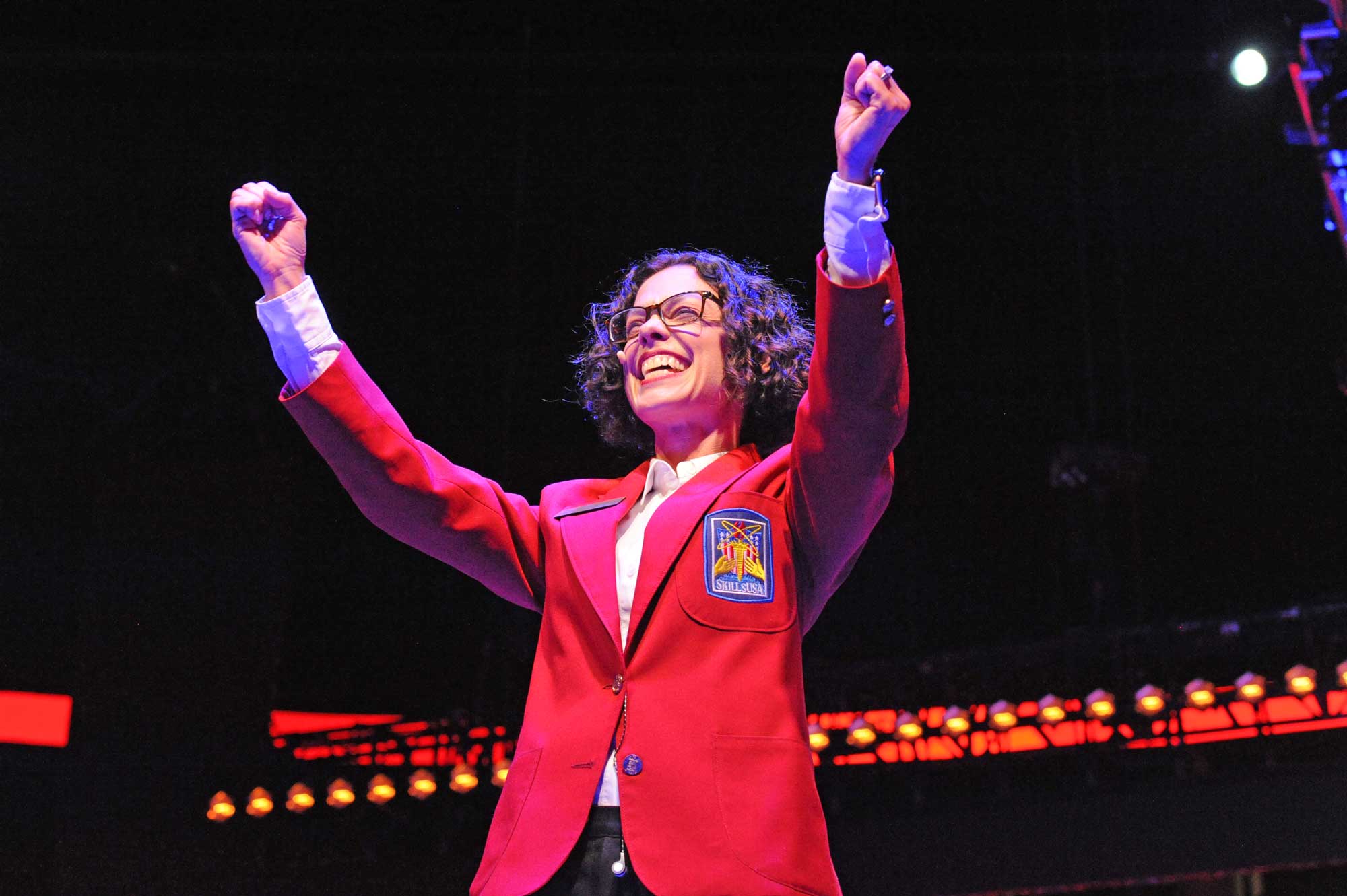 SkillsUSA Executive Director Chelle Travis on stage with hands raised.}