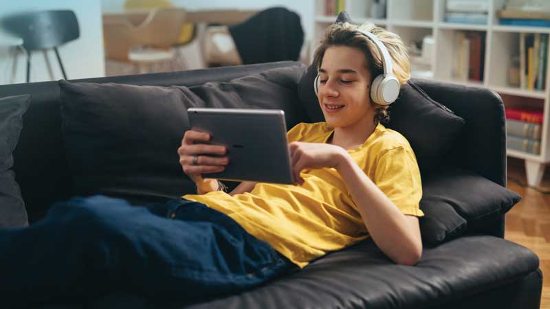 Smiling young man looking at a tablet. He is wearing headphones.