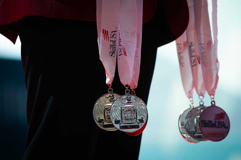 A group of SkillsUSA Championships medallions being held by someone wearing a SkillsUSA red blazer.