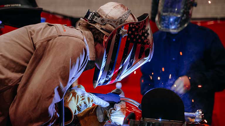 Welder welding with sparks flying. Another looks on.