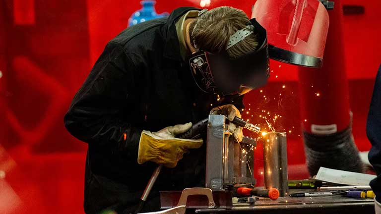 Person in welding gear, welding a piece of metal